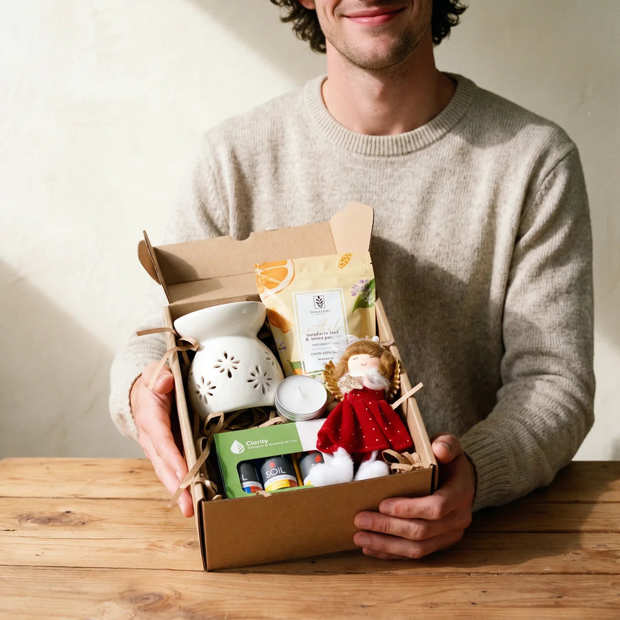 Smiling man holding out a kraft care box with an oil burner, essential oils and a plush angel, Fabulous Flowers South Africa