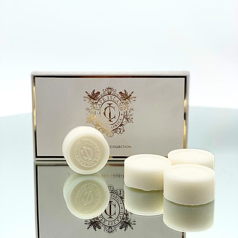 White soap bars with a decorative box featuring a logo on a reflective surface.