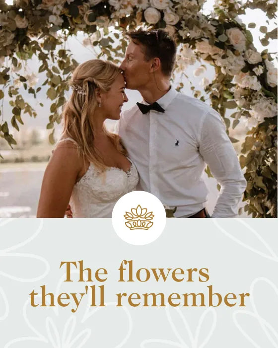 Couple in wedding attire standing under a floral arch with 'The flowers they'll remember' text.