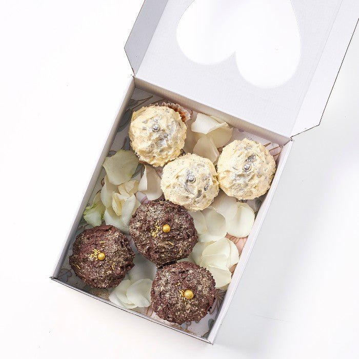 Elegantly arranged vanilla and chocolate cupcakes with golden toppings and white petal decorations in a white box, from Where Frosting Meets Fate collection.