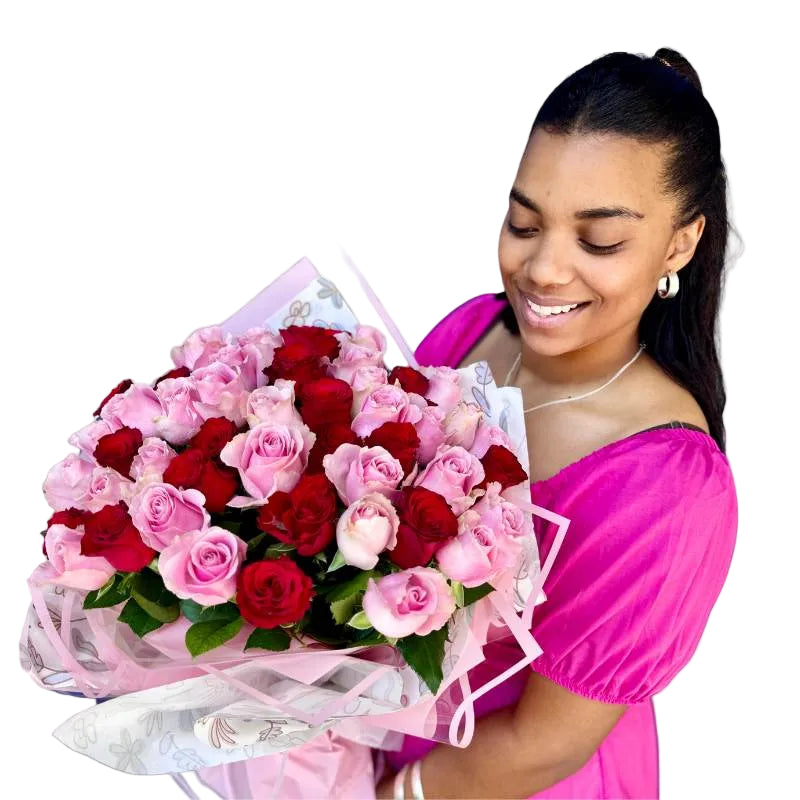 Smiling woman holding a bouquet of pink and red roses wrapped in delicate floral paper and pink ribbon by Fabulous Flowers & Gifts.