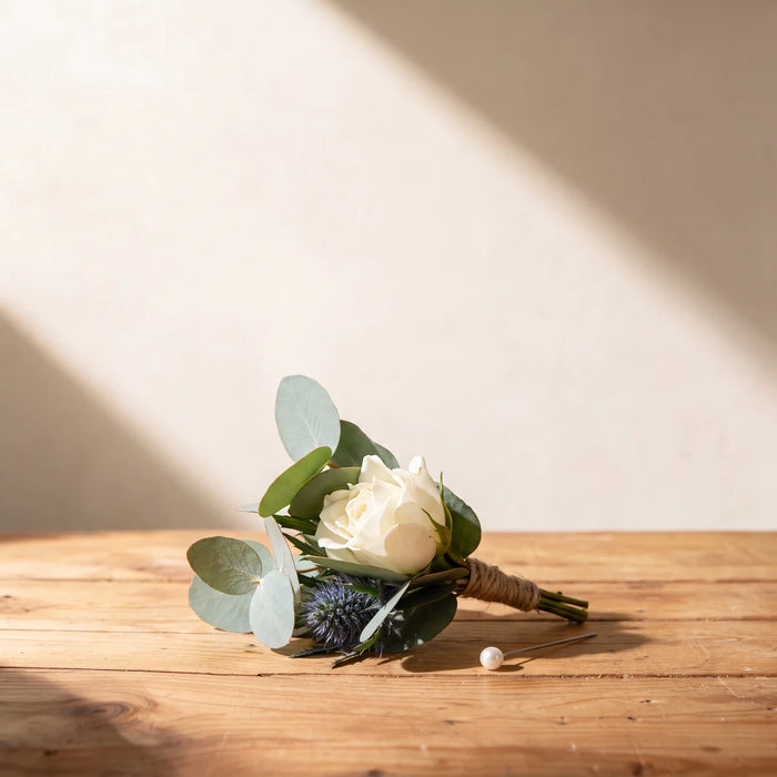 White rose, blue thistle and eucalyptus boutonniere tied with twine on a pine table, Fabulous Flowers South Africa