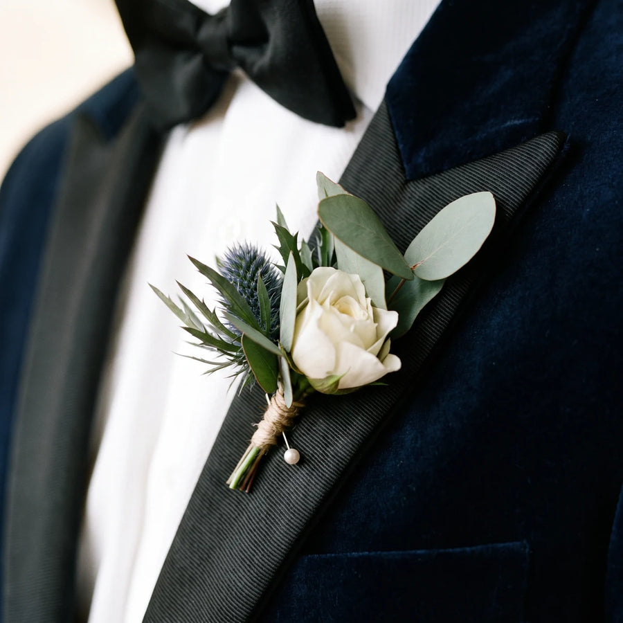 Close-up of an ivory rose, blue thistle and eucalyptus buttonhole on a satin lapel, Fabulous Flowers South Africa