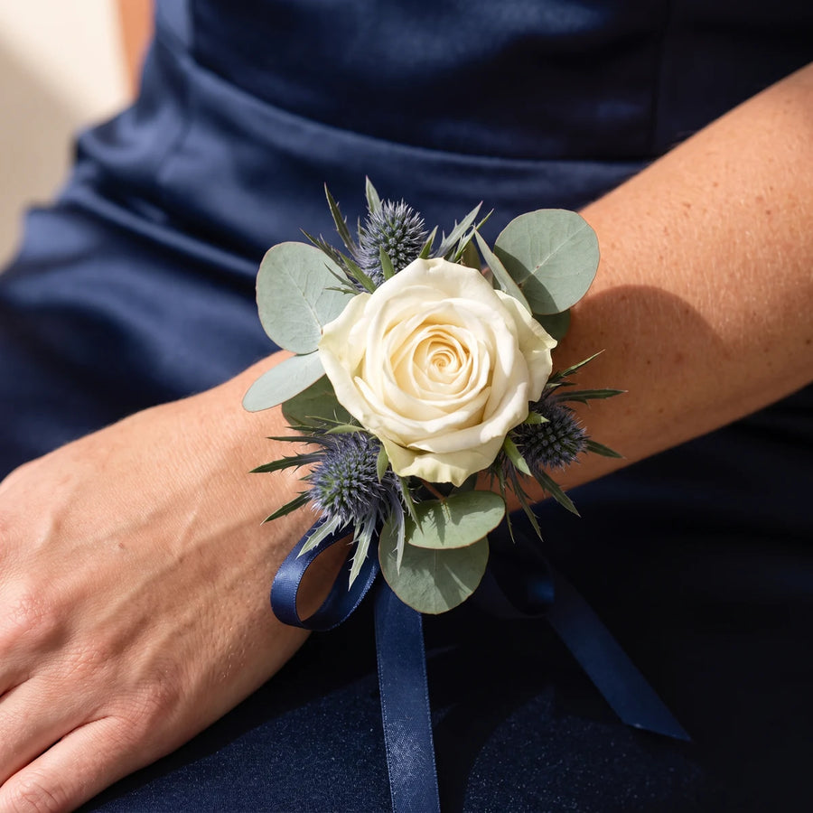 Close-up of a white rose and blue thistle corsage with navy ribbon on a wrist, Fabulous Flowers South Africa
