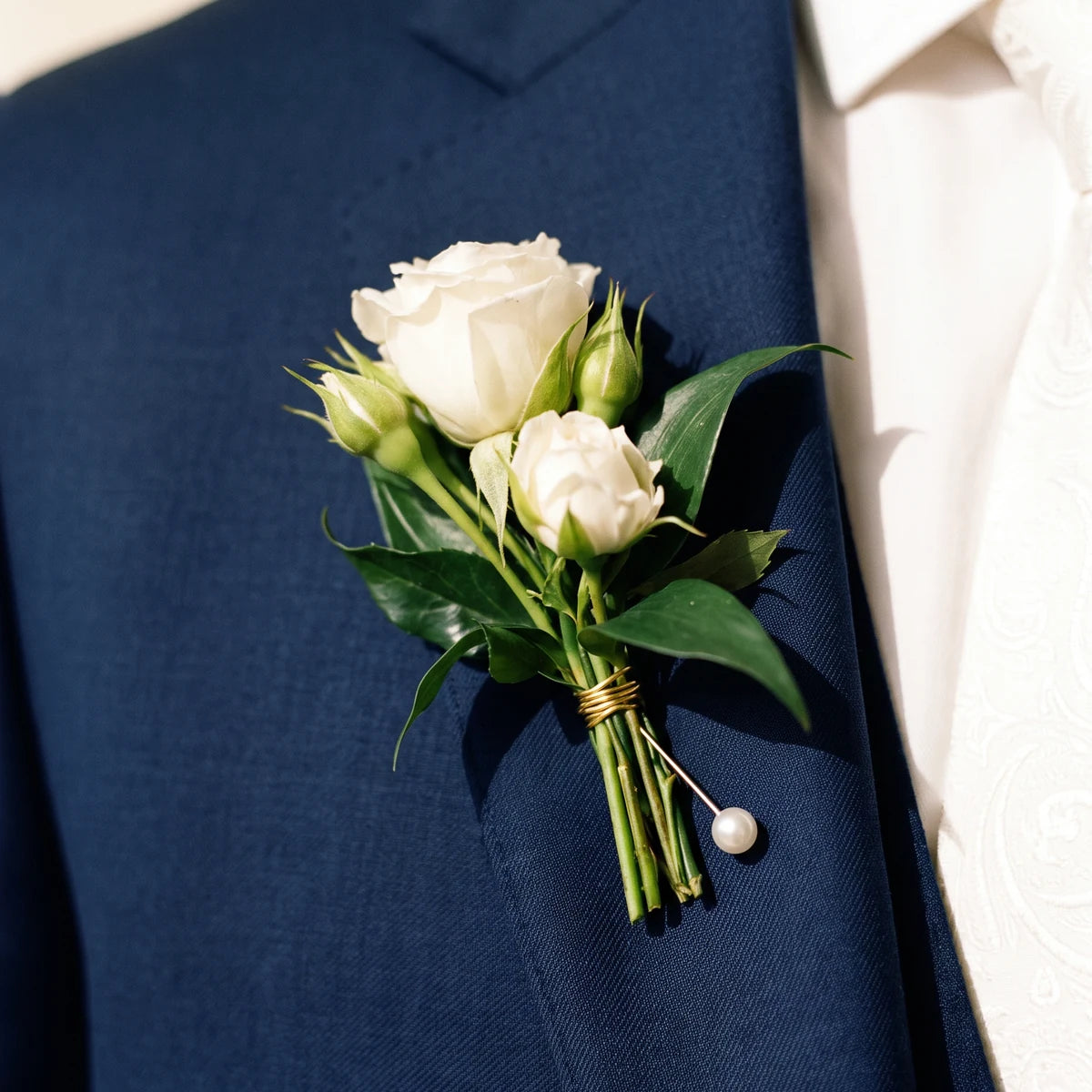 Close-up of white spray roses and ruscus bound in gold wire on a navy lapel, Fabulous Flowers South Africa