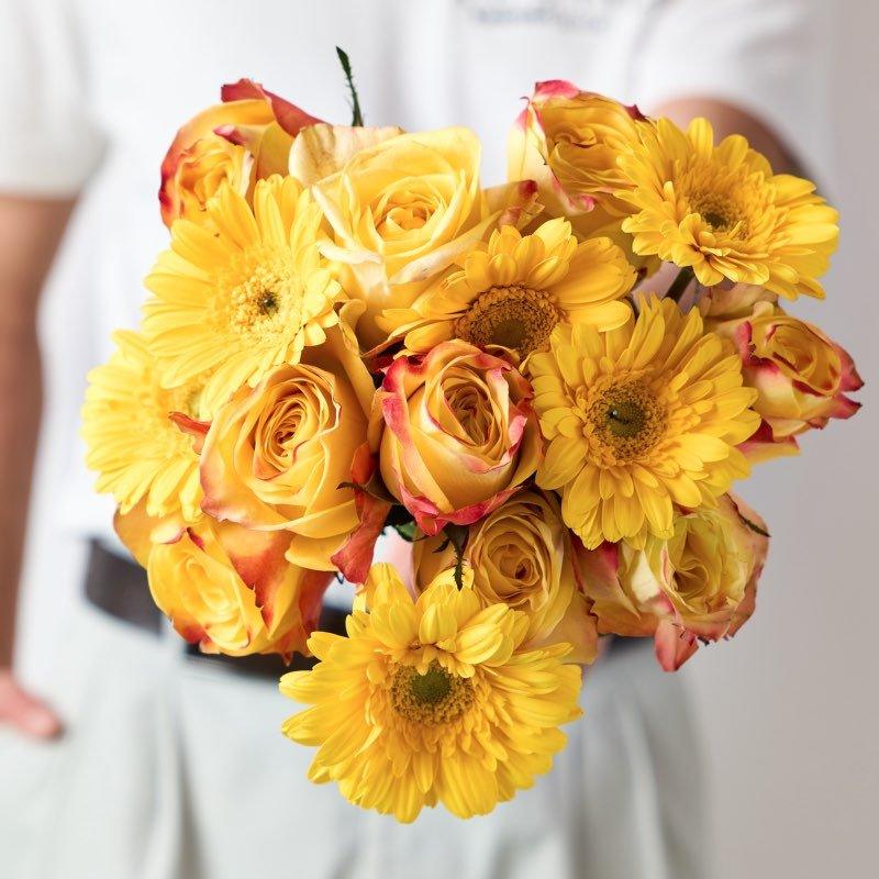 Bright yellow bouquet with roses and gerberas, held by florist in white – cheerful floral gift by Fabulous Flowers & Gifts