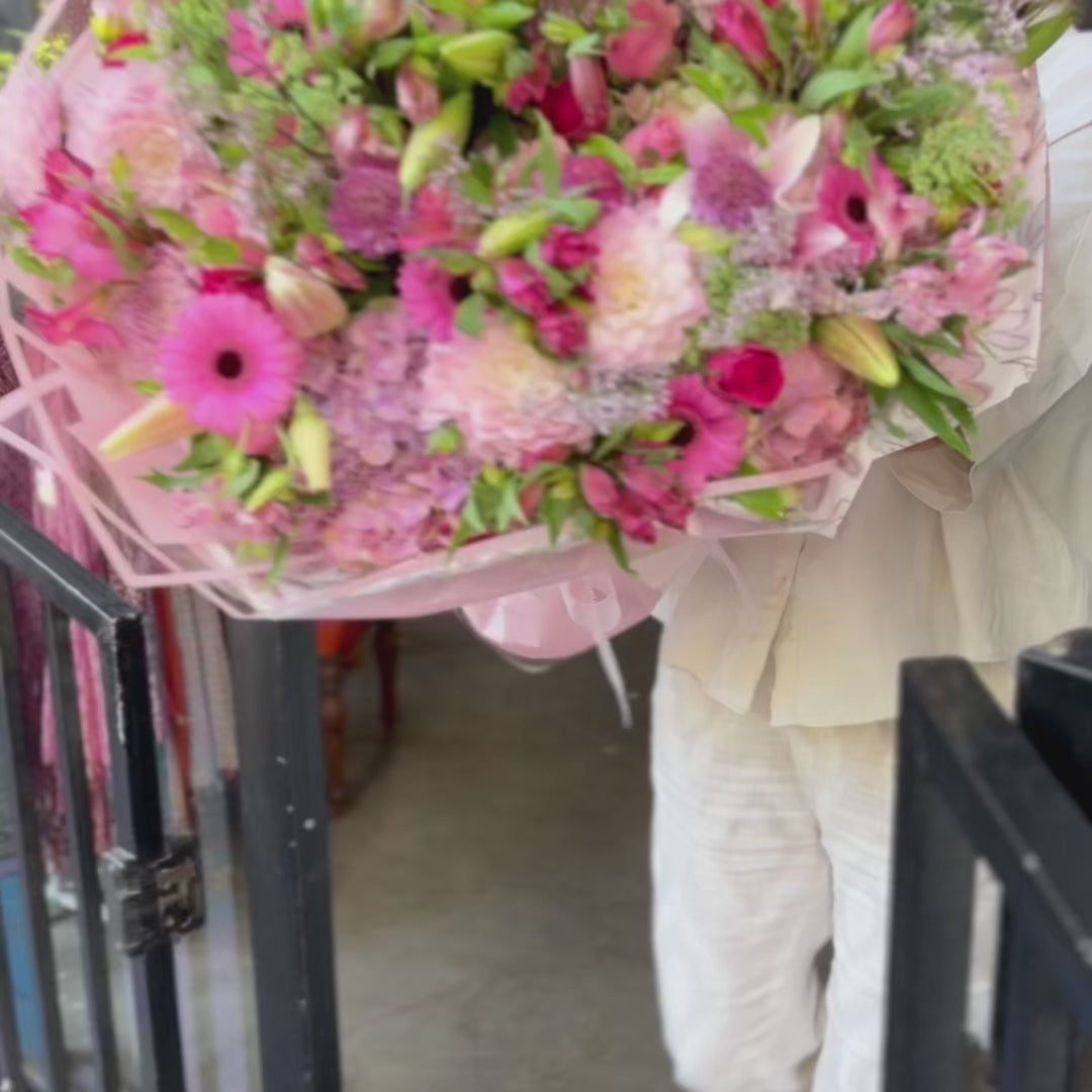 Video of a florist carryong and holding a beautiful big bouquet of pink flowers.
