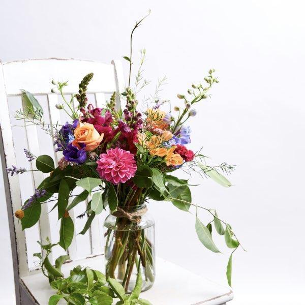 Glass jar vase arrangement with vibrant cheerful colours, seasonal dahlias, snapdragons, roses and alstroemeria 