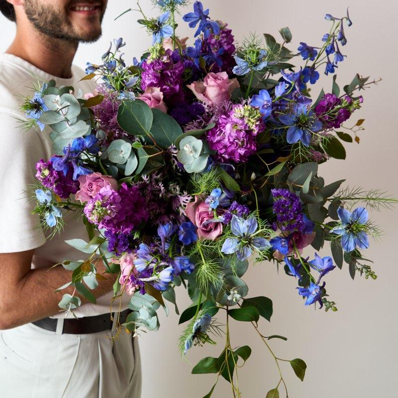 Luxury Lavender Garden Bouquet: Stunning mix of purple roses, blue delphiniums, and eucalyptus, held by smiling man