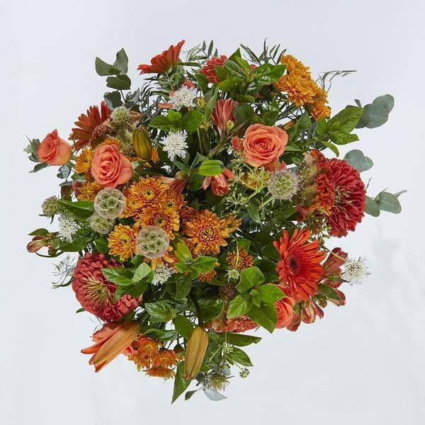 Orange roses, lilies, gerberas arranged with whimsical greenery in a glass vase