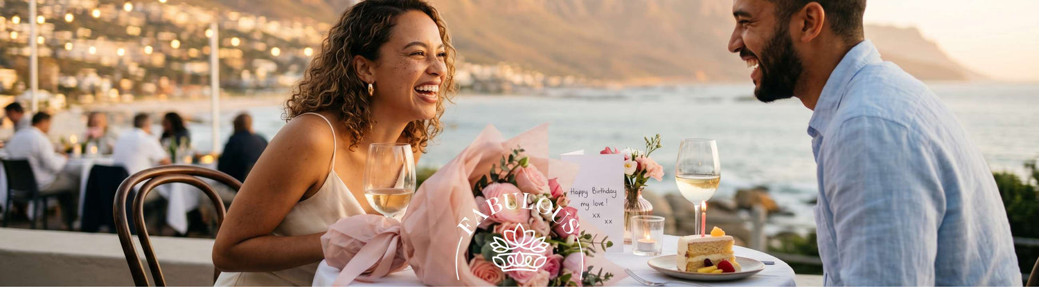 Couple celebrating her birthday at a Camps Bay sunset terrace with a pink-wrapped luxury bouquet from Fabulous Flowers and a handwritten Happy Birthday my love card