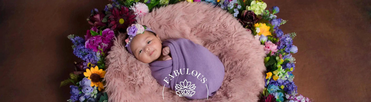 A serene baby swaddled in a purple blanket, surrounded by vibrant flowers on a fluffy pink cushion. Fabulous Flowers and Gifts.