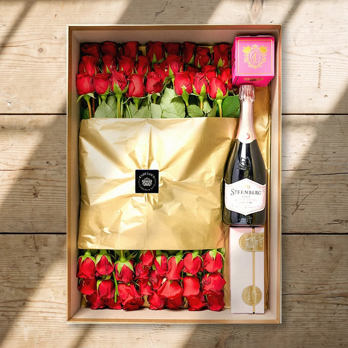Her Majesty's Gift Box from above on a pine table: 50 red roses, Steenberg Pinot Noir Cap Classique, a pink Cape Island candle and Frank & Olive fudge, Fabulous Flowers South Africa