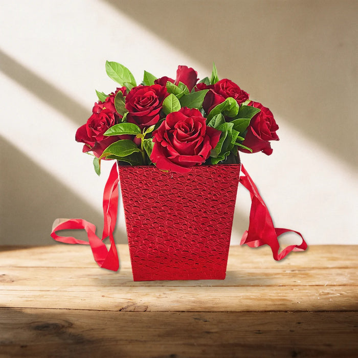 Red Rose Flower Box of 10 red roses with green leaves in a red textured box with ribbon handles on a sunlit pine table, Fabulous Flowers South Africa