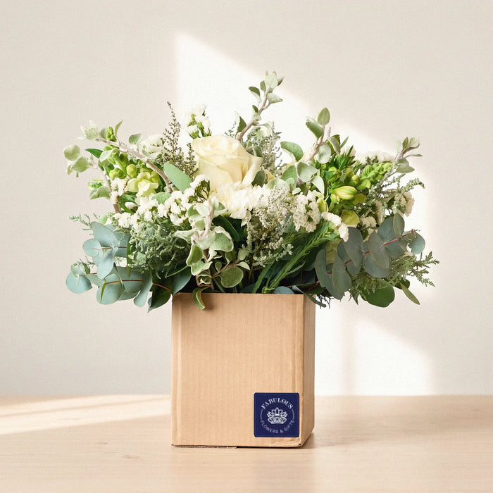 Kraft box of white and green flowers with a navy label on a pale pine table in morning sun, Fabulous Flowers South Africa