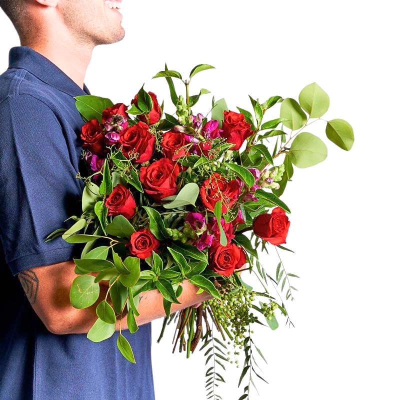 A Magical Love Story Bouquet with red roses and lush greenery held by a florist