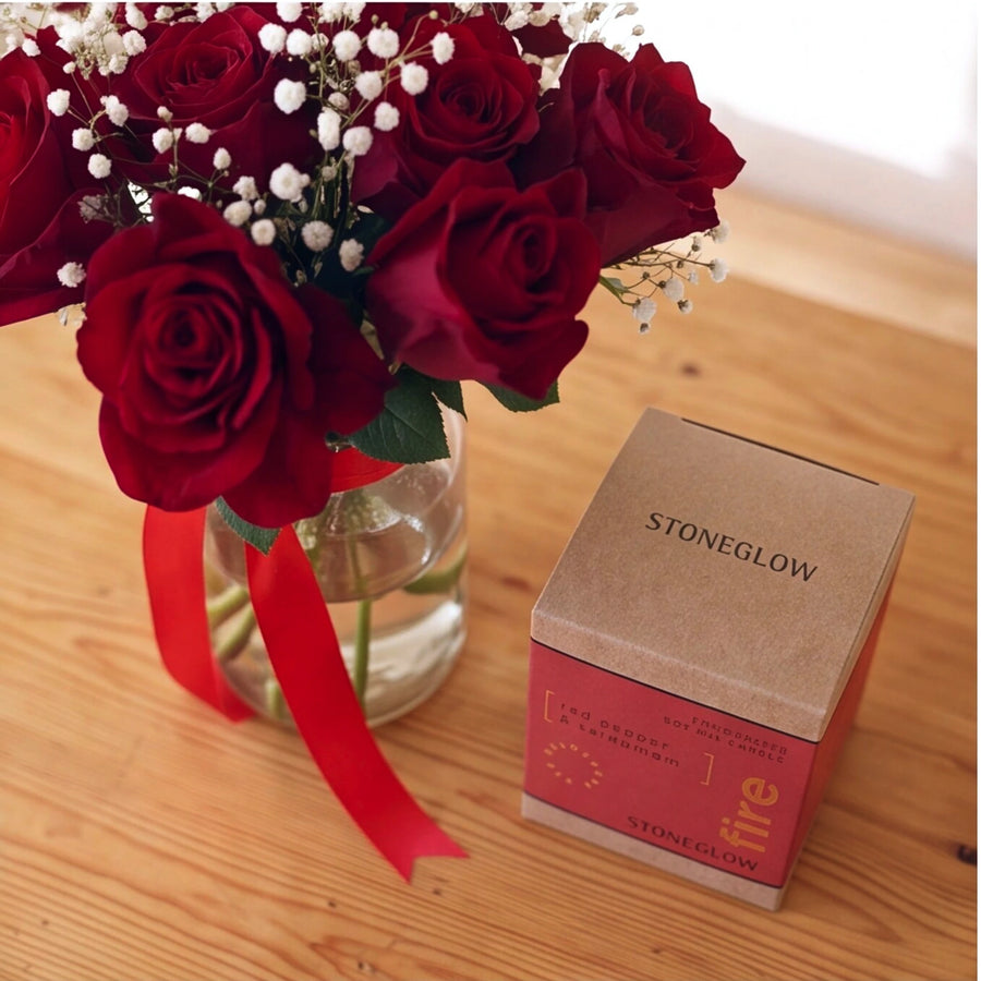 Deep red roses with white baby's breath beside a Stoneglow Red Pepper and Cardamom candle