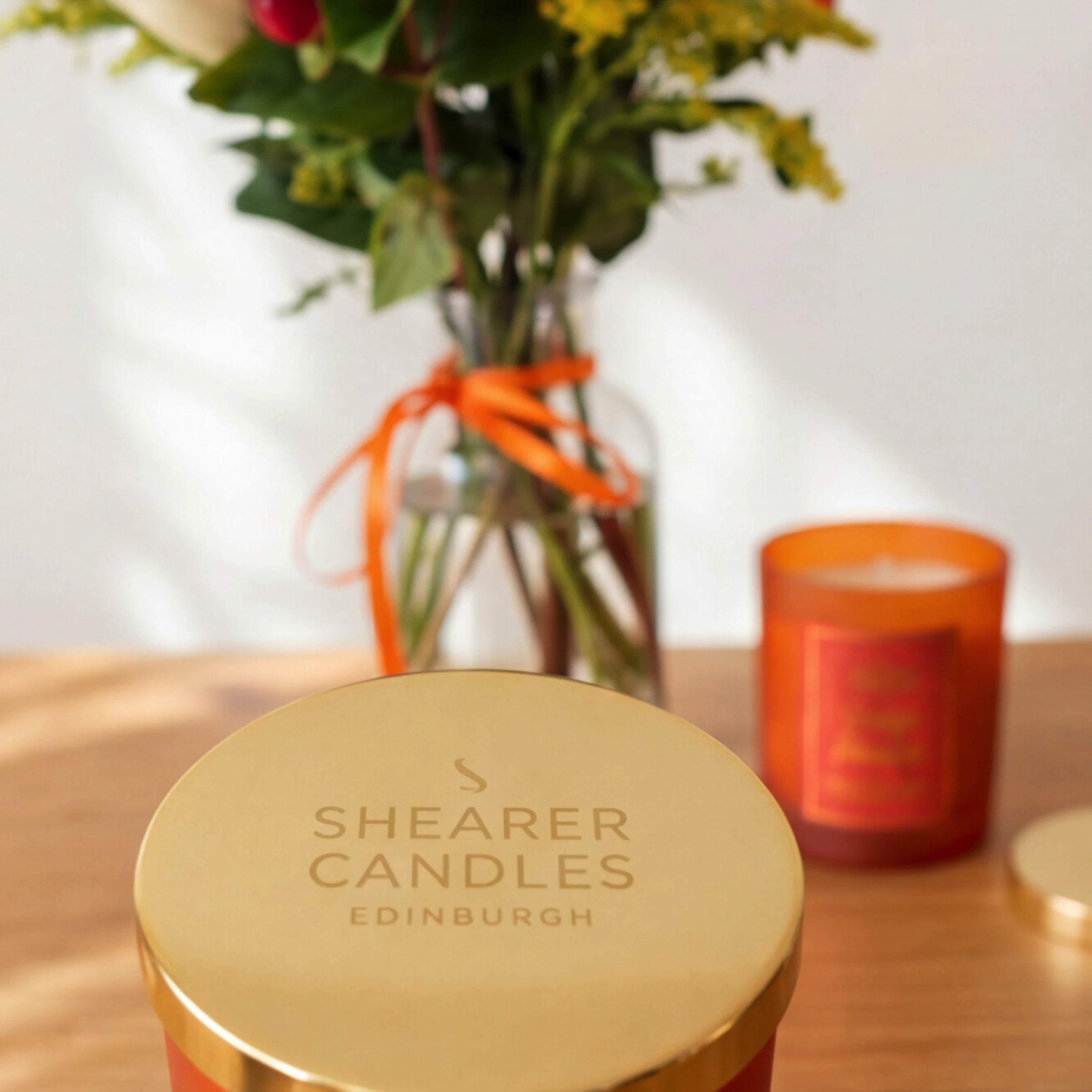 Shearer Candles Edinburgh gold lid with the Orange Pomander candle and Amber & Spice flowers behind