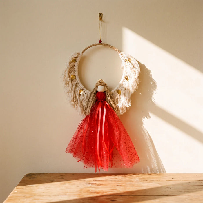 Handmade macramé Christmas angel with cream wings, gold leaves and a red tulle skirt hanging on a sunlit cream wall, Fabulous Flowers South Africa