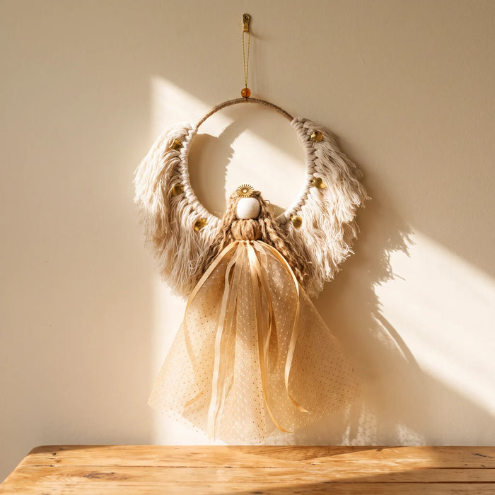 Handmade macramé Christmas angel with cream wings, gold leaves and a champagne-gold tulle skirt hanging on a sunlit cream wall, Fabulous Flowers South Africa