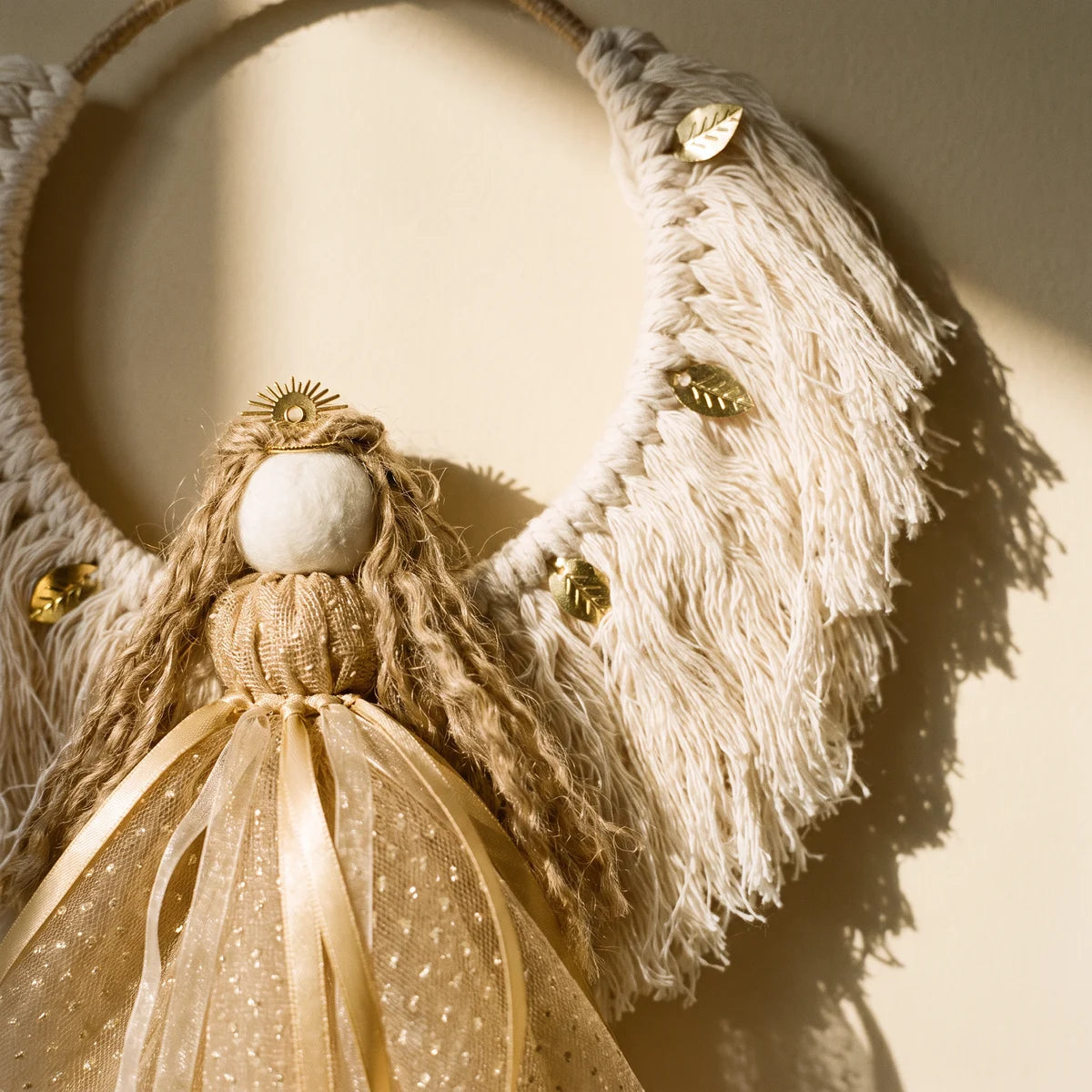 Close-up of a macramé angel's white felt face, gold crown, jute hair and cream wings with gold leaves above a champagne-gold skirt, Fabulous Flowers South Africa