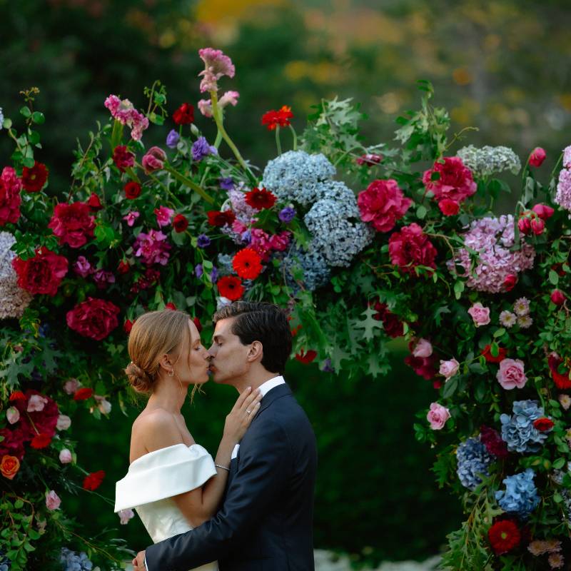 Bride and groom kissing under colourful flower arch on their wedding day in Constantia - Fabulous Flowers
