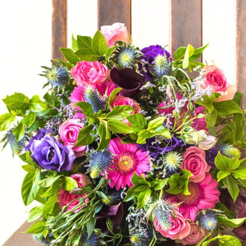Bouquet of colorful flowers including pink roses and purple and green foliage on a wooden surface.