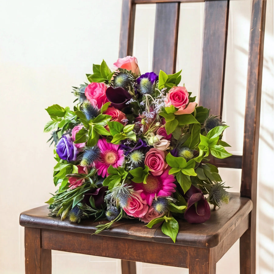The Berry Bloom bouquet of purple and pink flowers, angled in warm sunlight
Top-down view of Berry Bloom, pink roses, purple lisianthus, gerberas and blue thistle