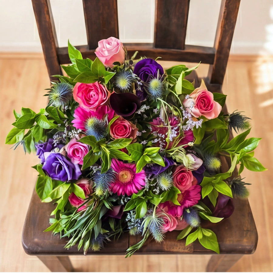 The Berry Bloom purple and pink flower bouquet on a wooden chair in a sunlit room