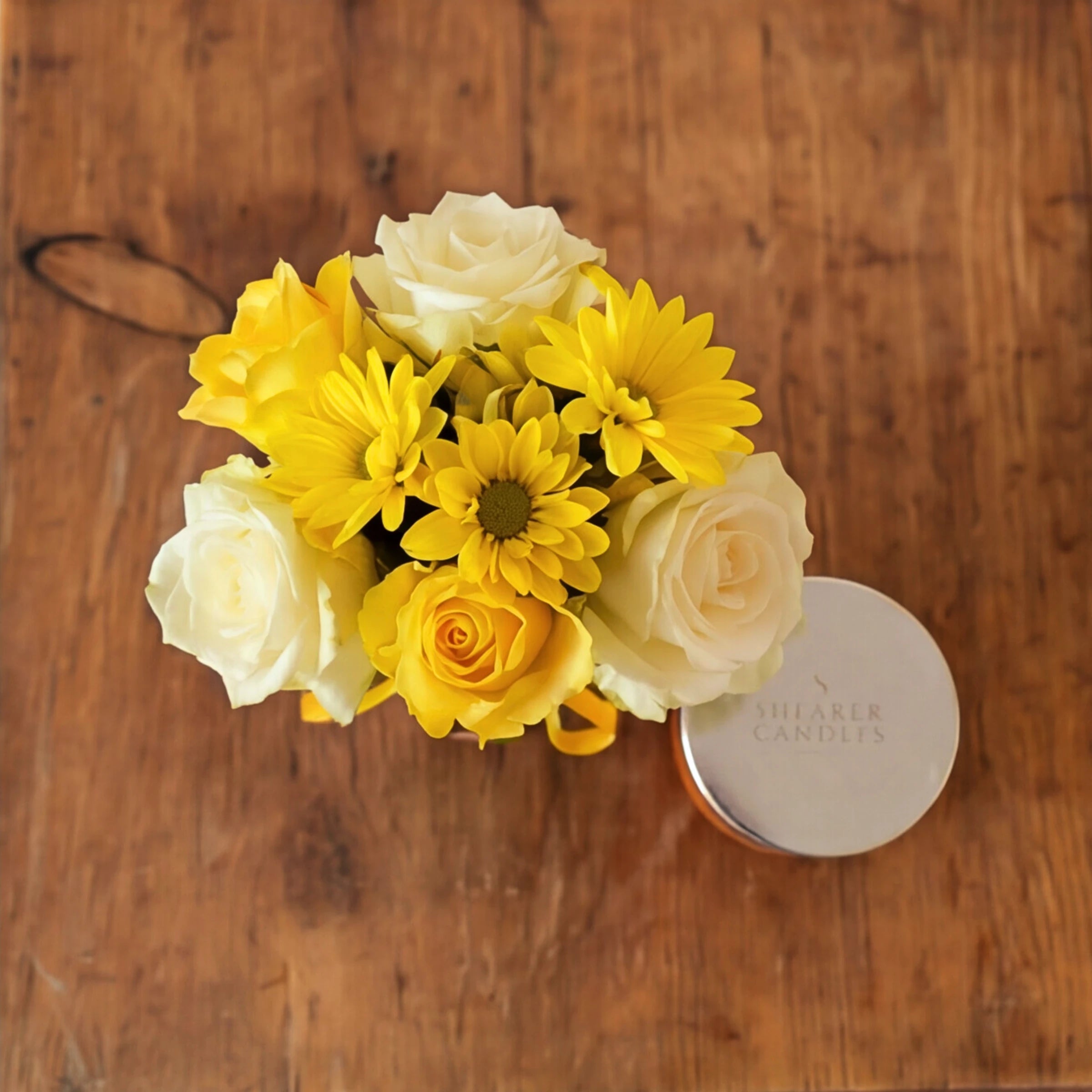 Top-down view of the Bloom & Glow posy of yellow and cream roses beside the Shearer Candles candle