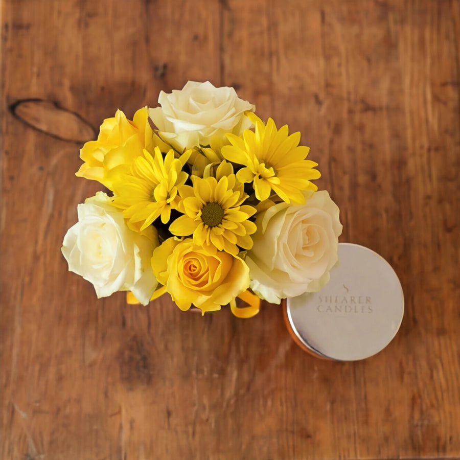 Top-down view of the Bloom & Glow posy of yellow and cream roses beside the Shearer Candles candle