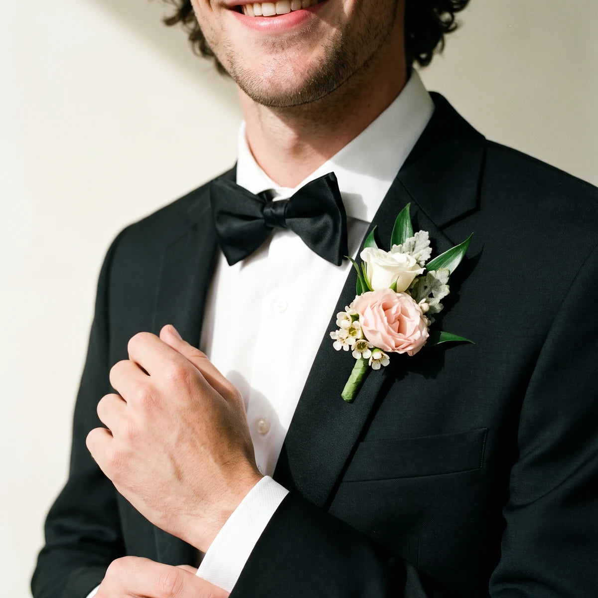 Man in a black tuxedo adjusting his cuff while wearing a blush rose boutonniere, Fabulous Flowers South Africa