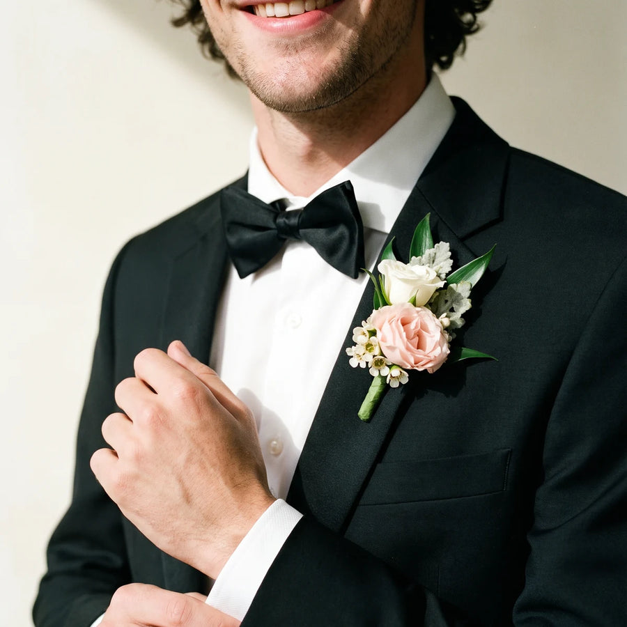 Man in a black tuxedo adjusting his cuff while wearing a blush rose boutonniere, Fabulous Flowers South Africa