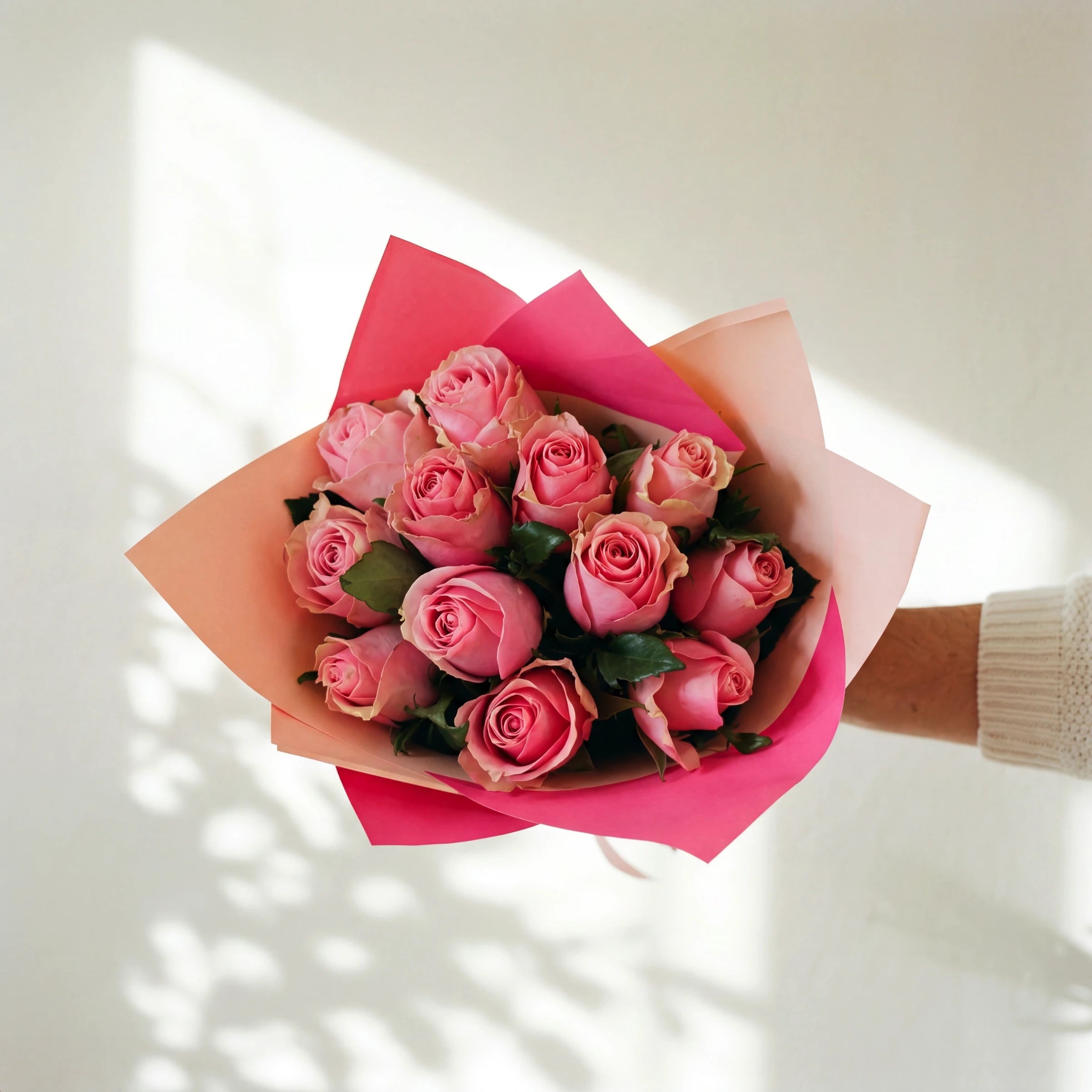 Bonbon, a dozen pink roses in a two-tone pink and peach wrap, held by Fabulous Flowers