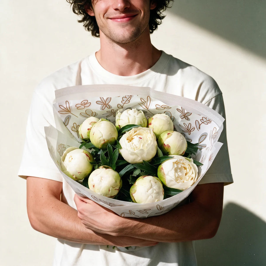 Man with curly dark hair in a white t-shirt holding a bouquet of ten Bowl of Cream peonies in warm sunlight, Fabulous Flowers South Africa