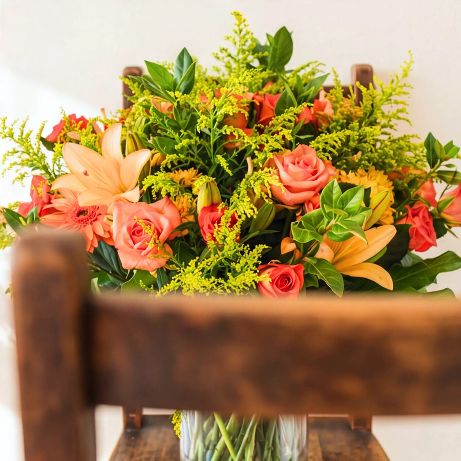 The Bright Orange Glass Vase of orange and coral flowers on a wooden chair in the sun