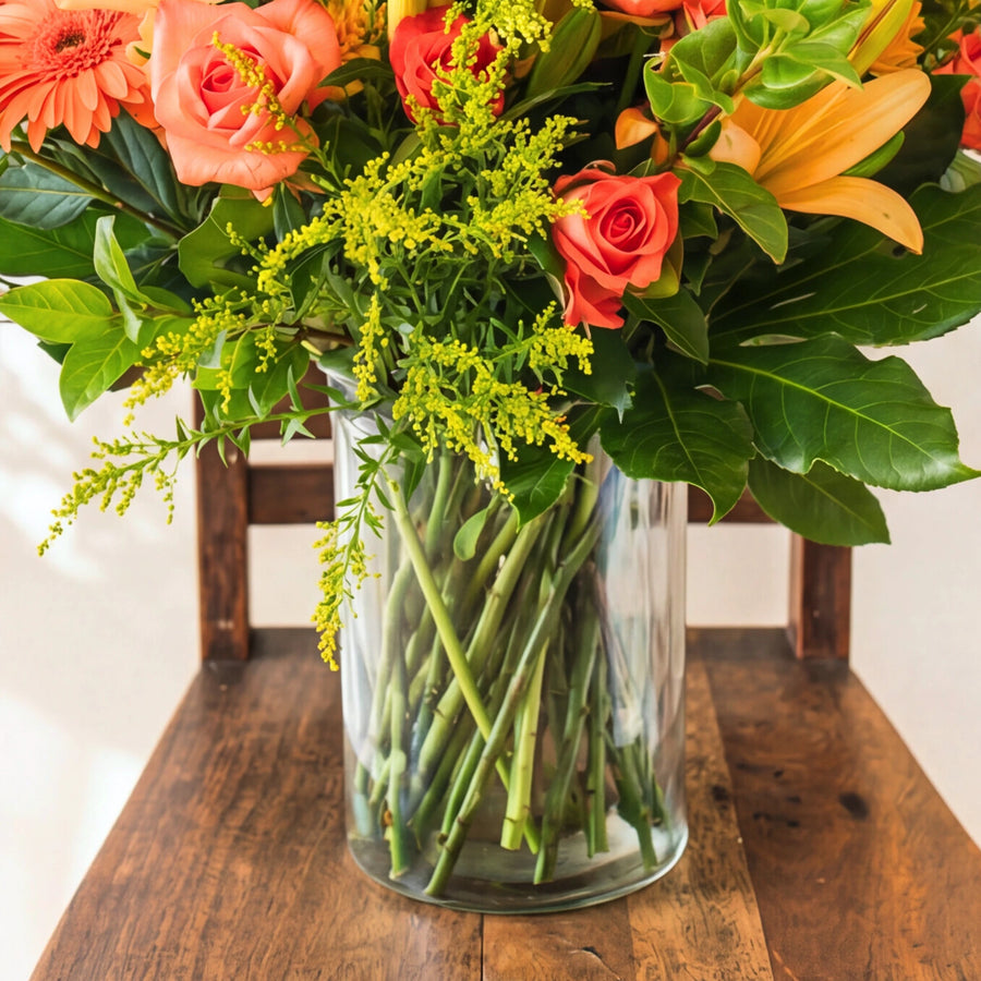 Green stems in the clear glass vase with orange roses, lily and solidago above