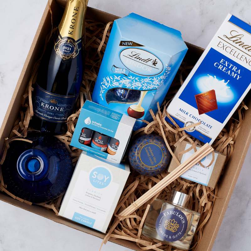 Close-up of Bubbles & Bliss Treat Box featuring Krone champagne, Lindt chocolates, essential oils, soy candle, and Fabulous Flowers & Gifts reed diffuser in a luxurious gift box.