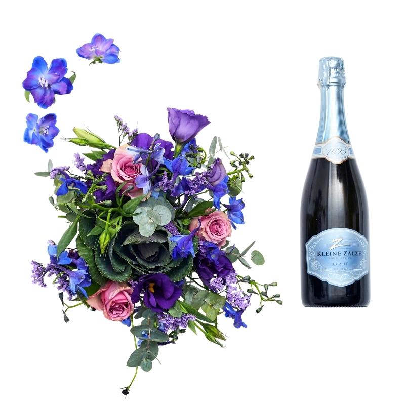 Close-up blue and lilac blooms in vase with greenery, paired with a bottle of bubbly