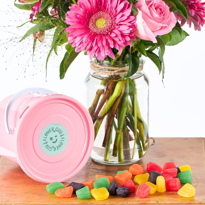 Pink mug with a floral arrangement and colorful candies on a wooden surface