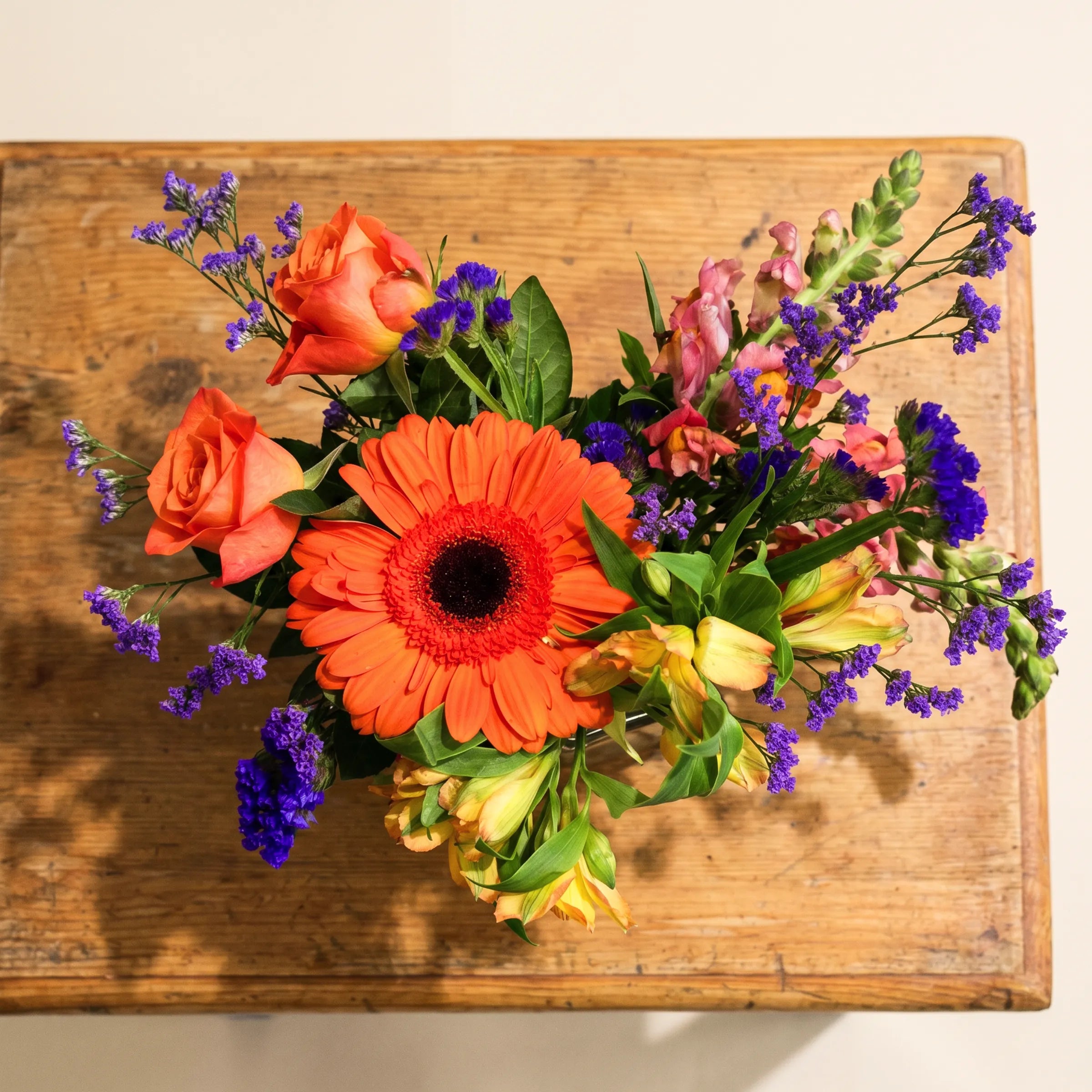 Close-up of the orange gerbera daisy at the centre of Carnival in a Jar by Fabulous Flowers South Africa, the cheerful focal flower paired with peach roses, pink snapdragons and purple statice in the small glass jar