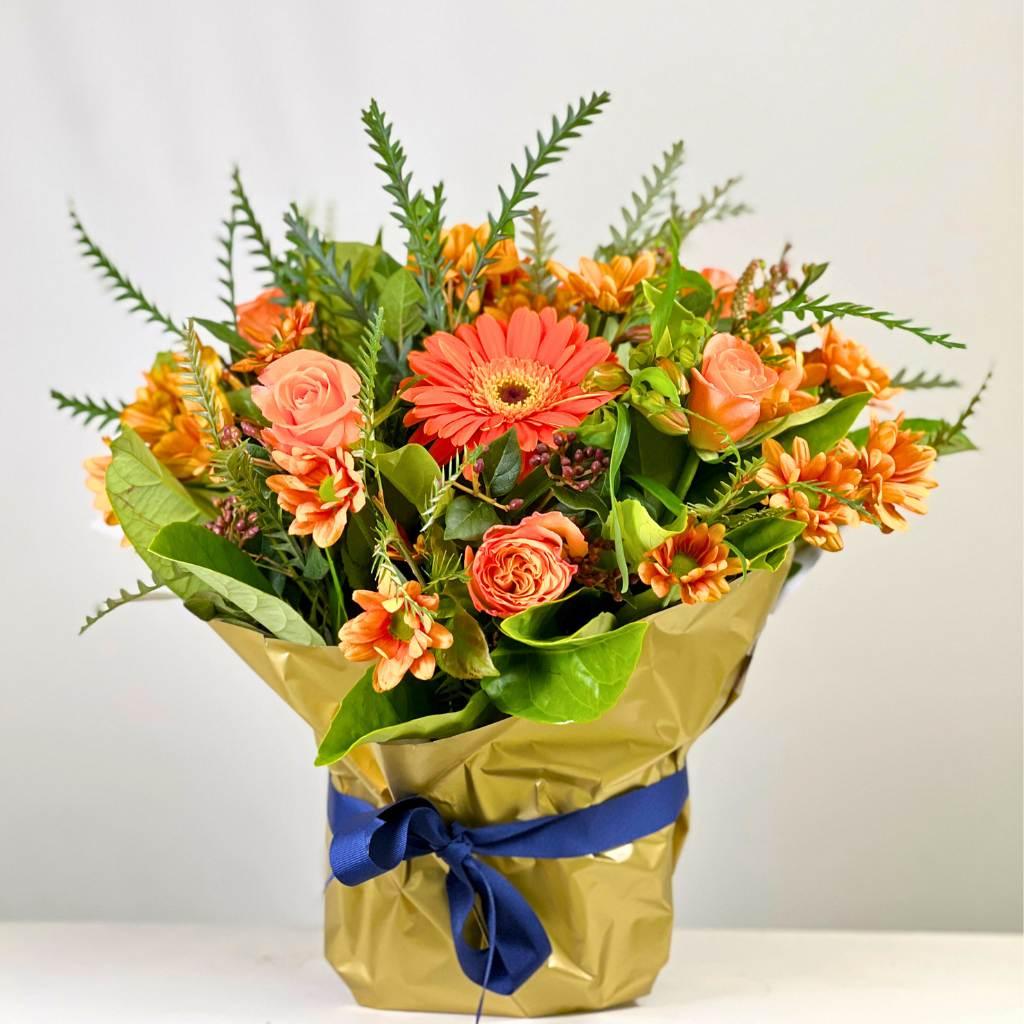 Celebrate Flower Arrangement with mixed orange flowers wrapped in gold paper and a blue ribbon - Fabulous Flowers