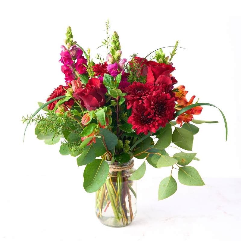 Arrangement of red and pink flowers in a clear vase on a white background