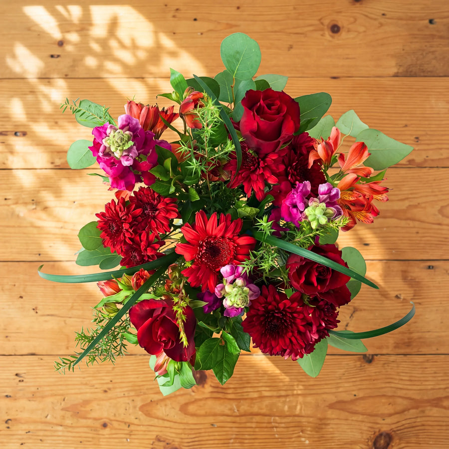 Overhead of the Charming red flower arrangement, red roses, chrysanthemums, orange alstroemeria and eucalyptus in a glass jar