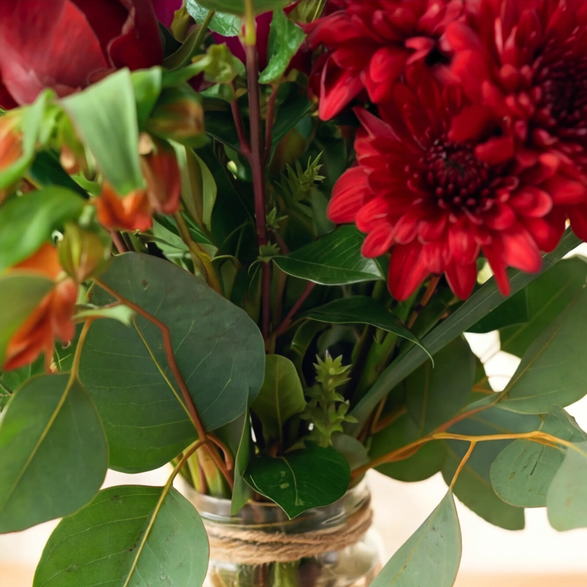 Detail of the Charming arrangement in its twine-wrapped glass jar, red chrysanthemums, orange alstroemeria and eucalyptus