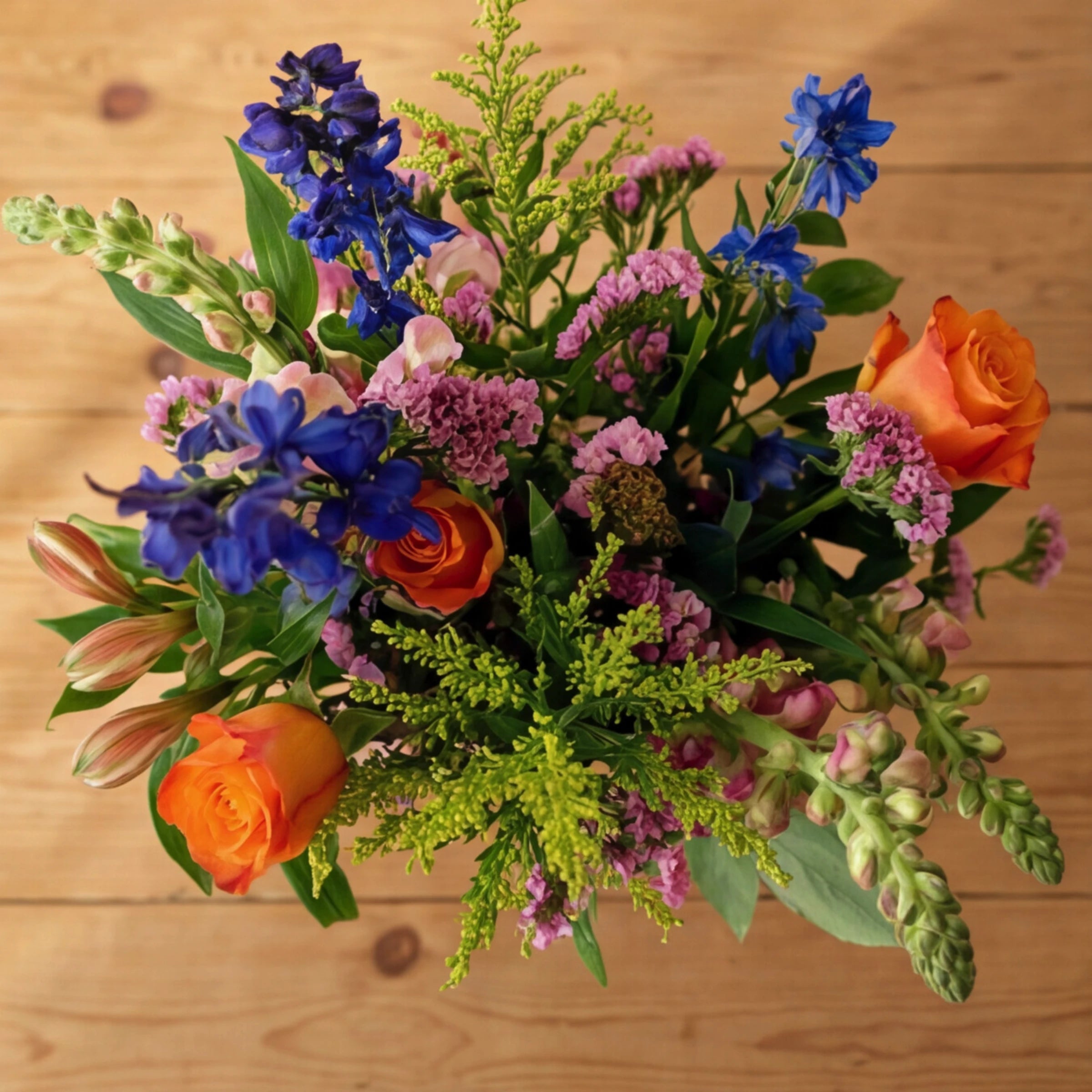 Top-down view of Cheer in a Jar, orange roses, blue delphinium, pink limonium and lime solidago, Fabulous Flowers