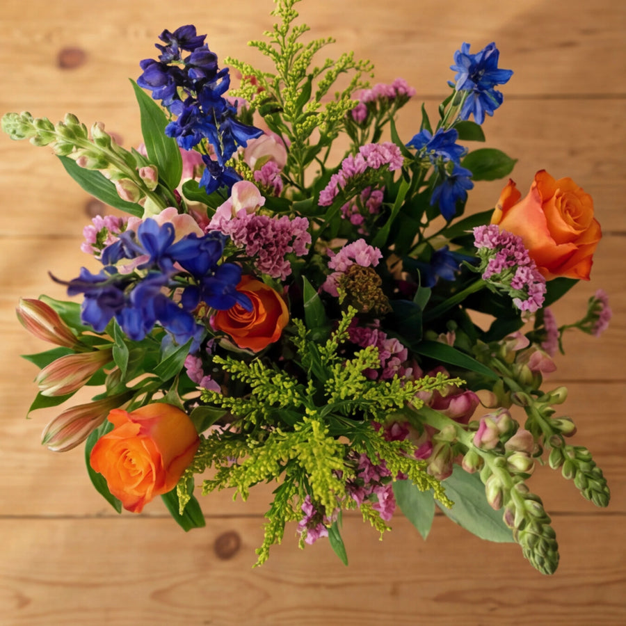 Top-down view of Cheer in a Jar, orange roses, blue delphinium, pink limonium and lime solidago, Fabulous Flowers