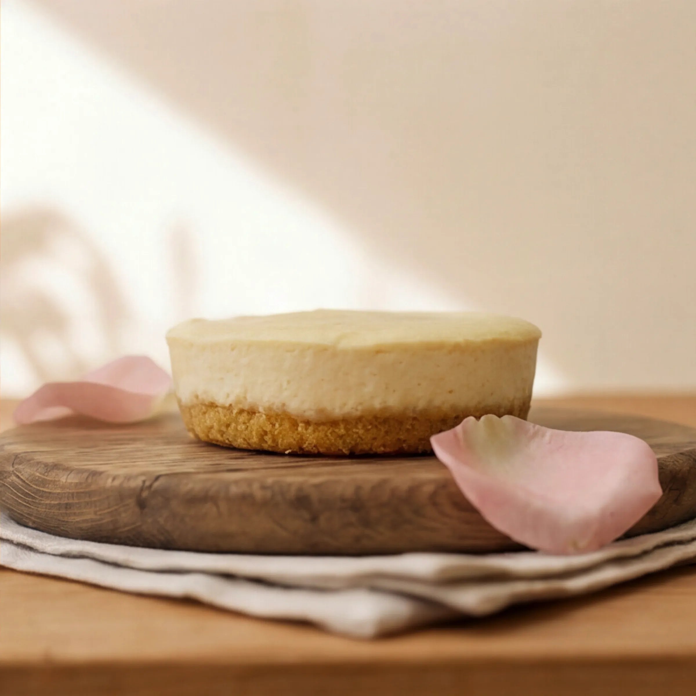 Side view of single-portion Lemon Cheesecake with golden biscuit base on oak board by Fabulous Flowers