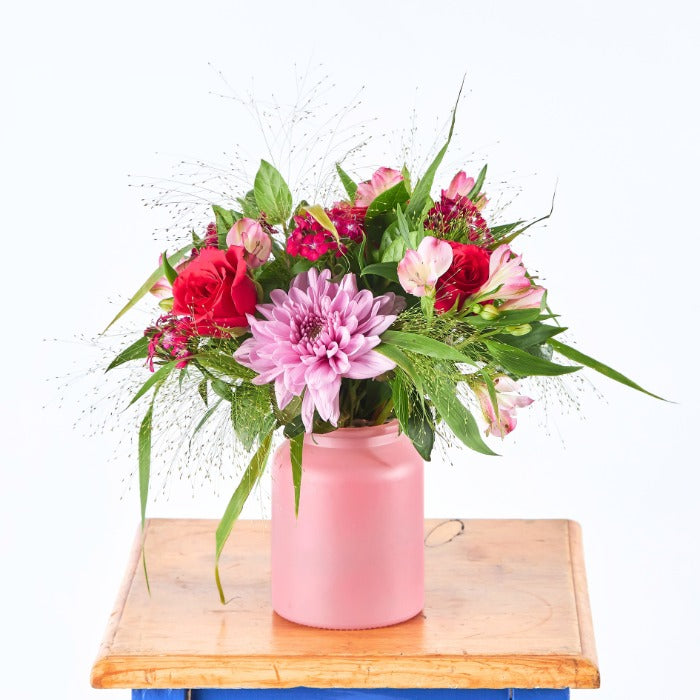 Cherry Bombshell by Fabulous Flowers & Gifts – bold pink and red blooms with greenery in a matte pink vase on wooden table