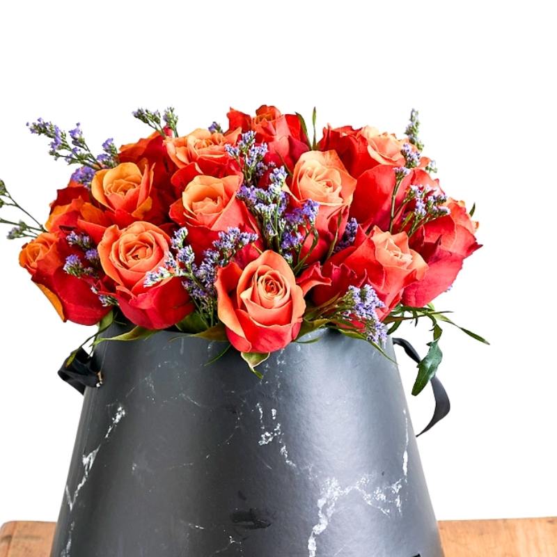 Arrangement of red and orange roses in a gray black marble vase on a white background